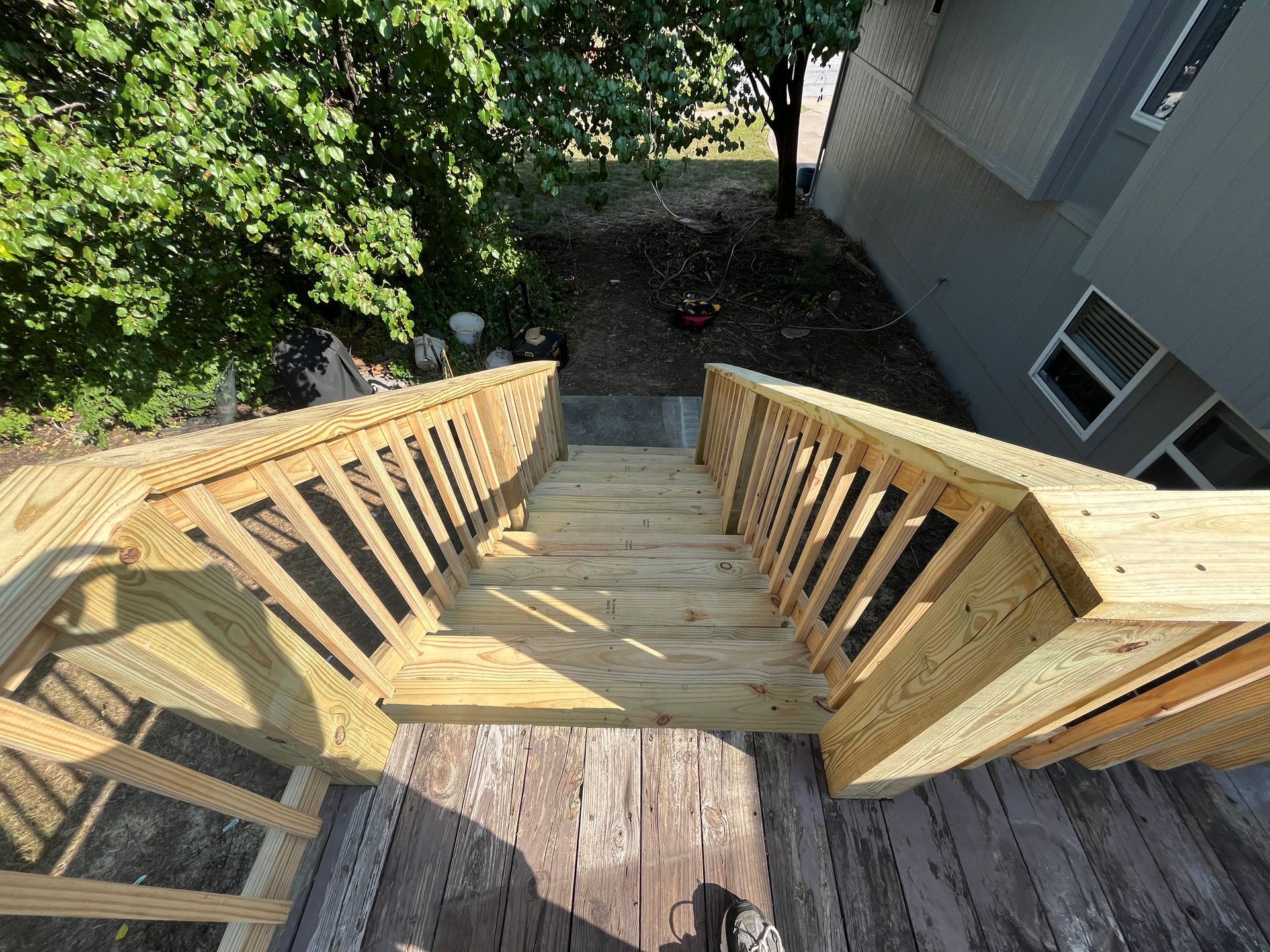 Wooden staircase with railing leads down to a yard; view from above.