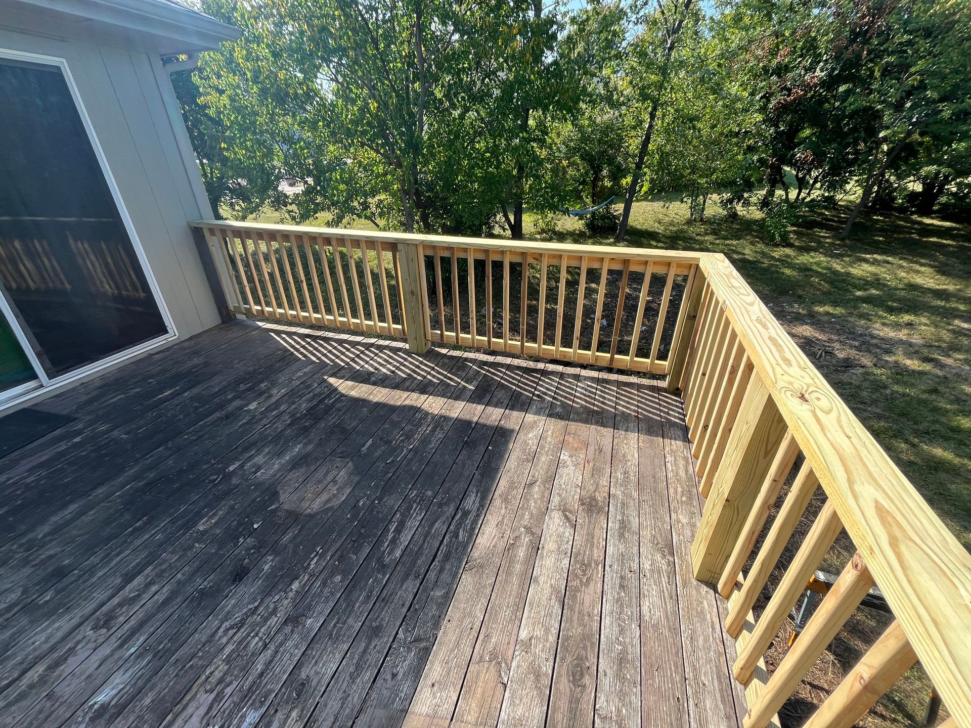 Wooden deck with new light brown railing, old weathered wood, and trees in background.