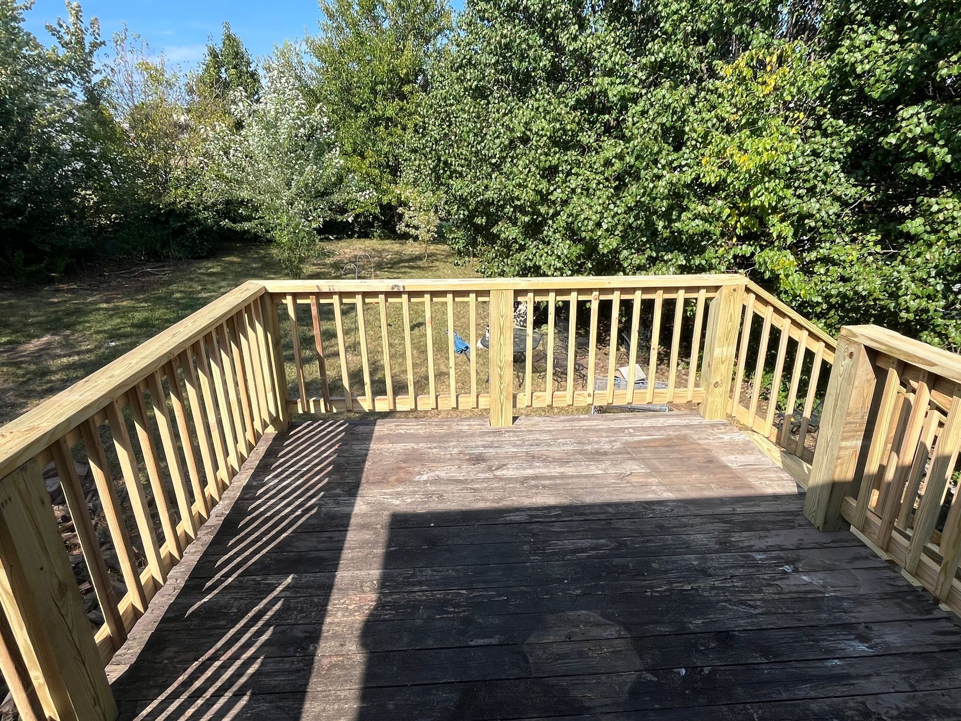 Wooden deck with railing, leading to a grassy area with trees and blue sky.