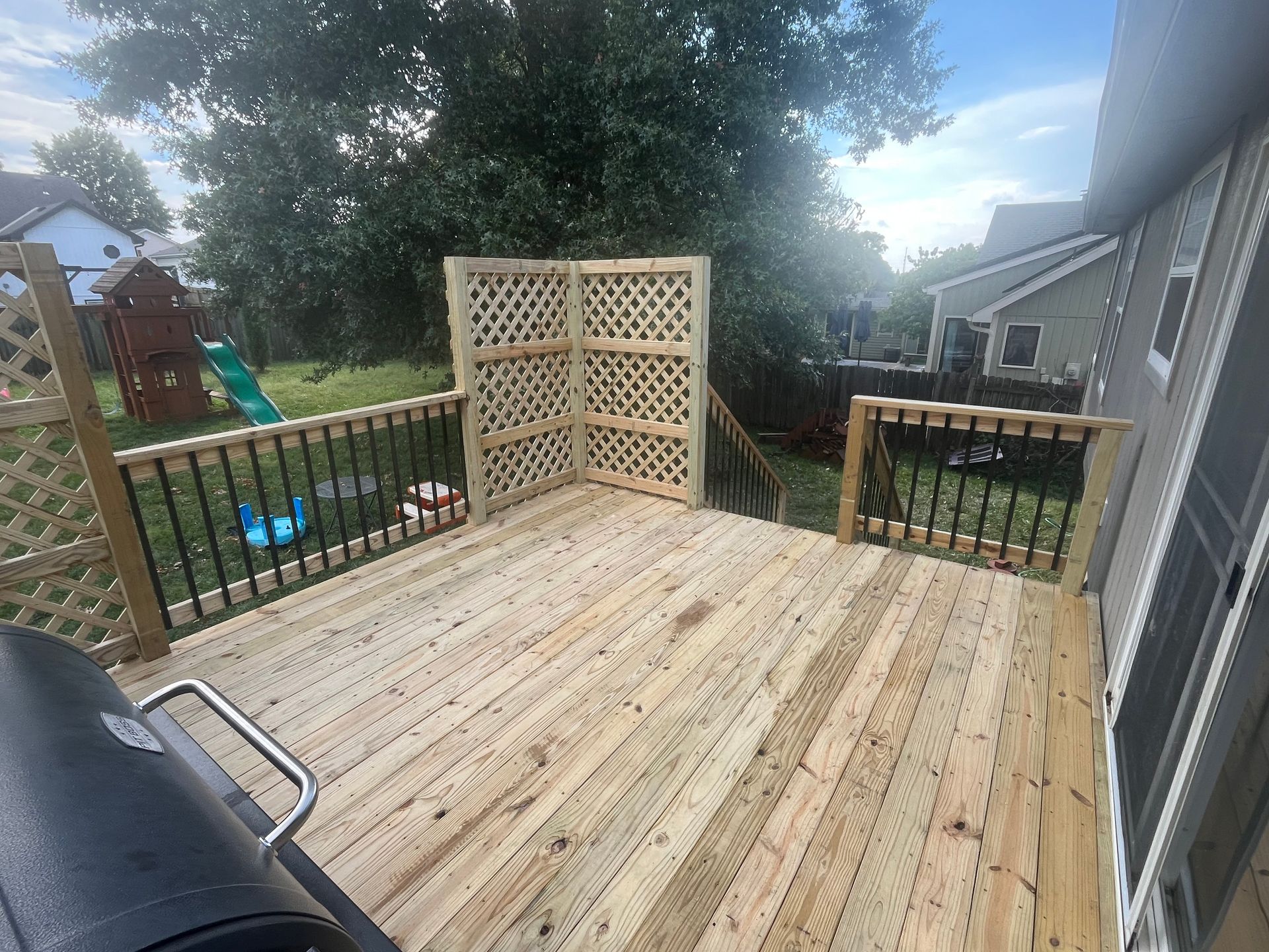 Wooden deck with black railings and lattice screen.