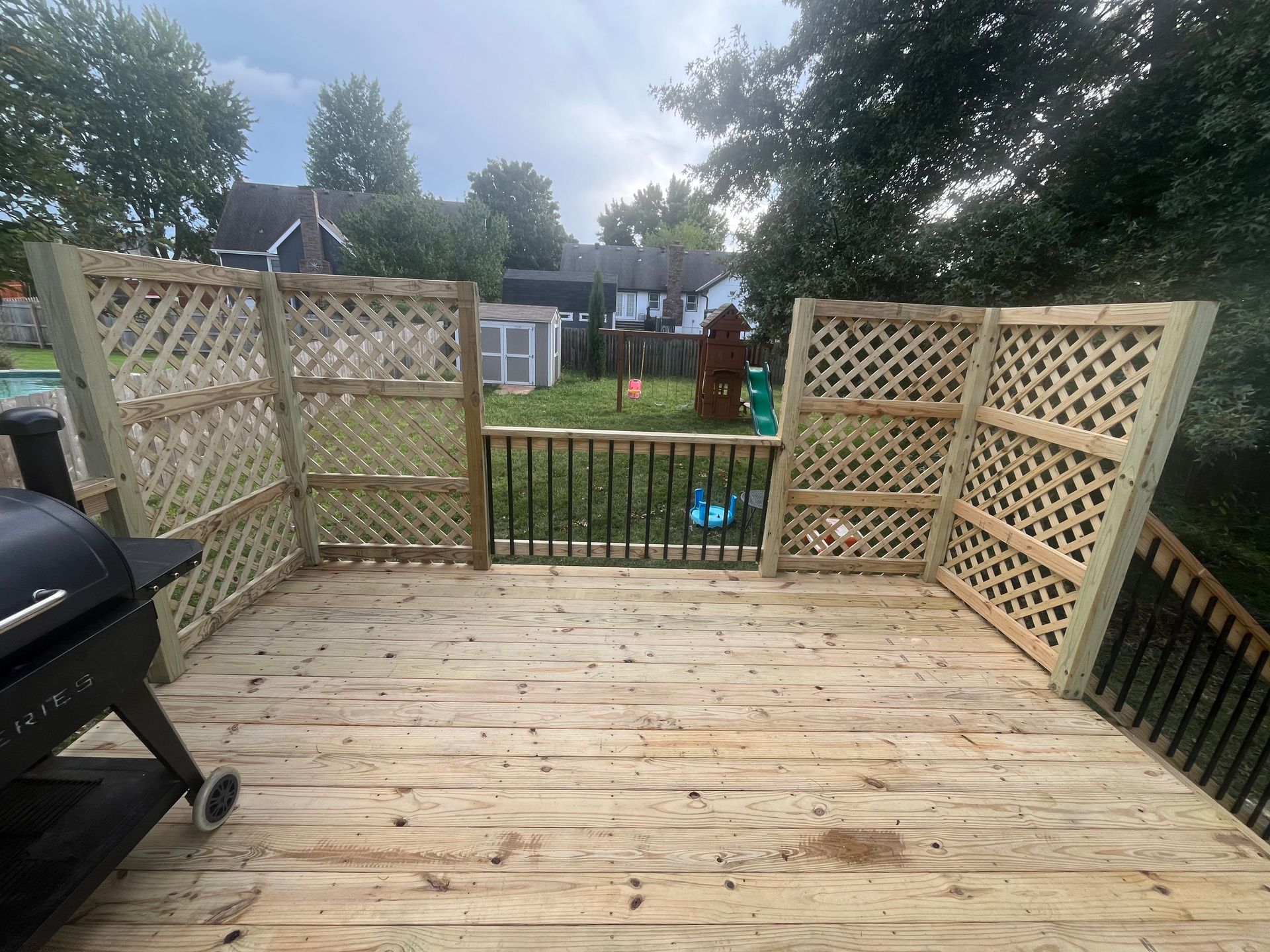 Wooden deck with lattice panels, barbecue grill, and view of a yard with a play set.
