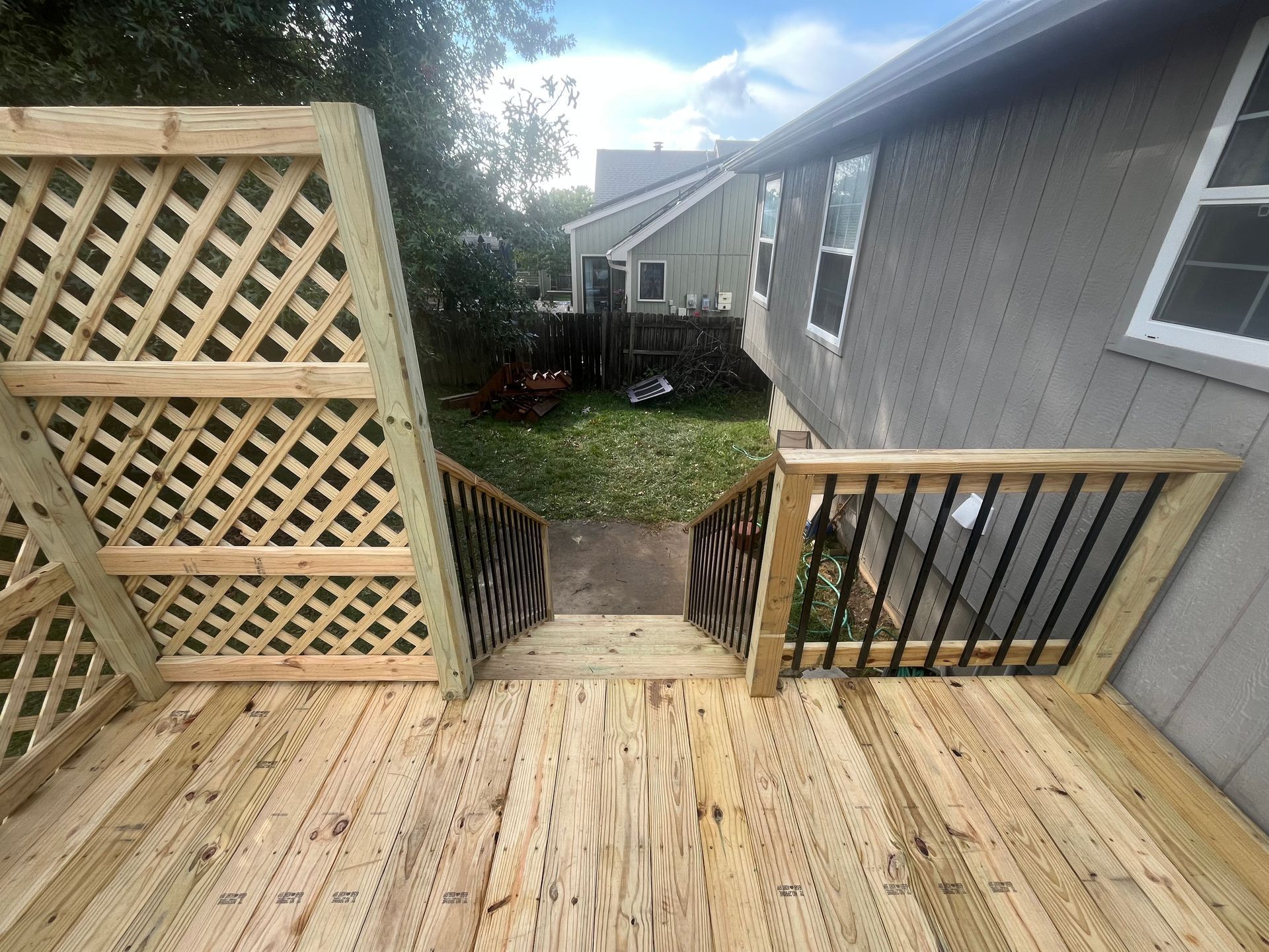 Wooden deck with lattice panels, stairs, and railing leading to a grassy yard.