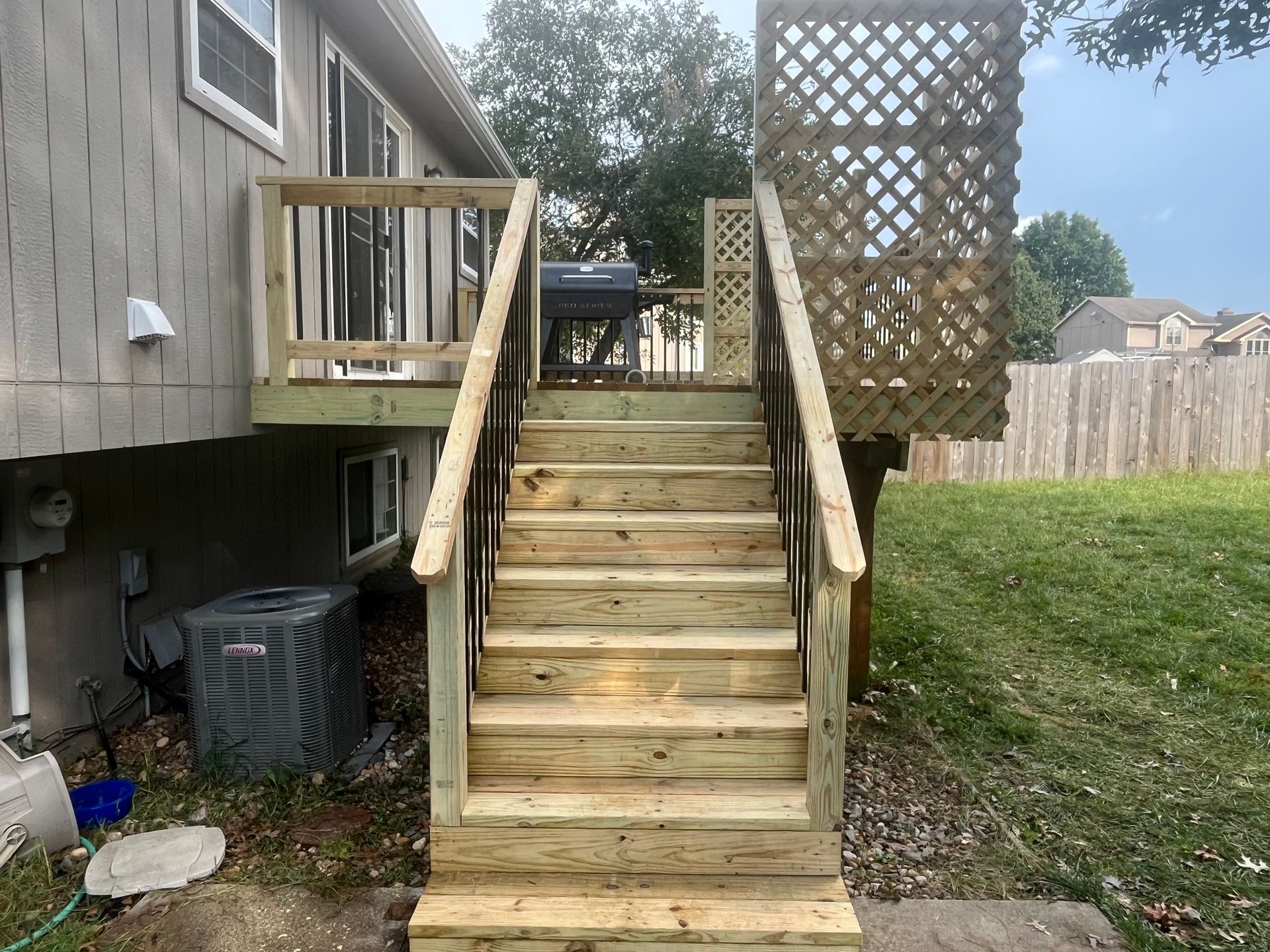 Wooden deck with stairs leading to a backyard, with a trellis on the right.