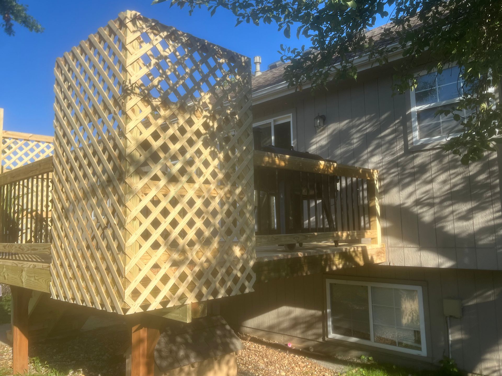 Wooden deck with lattice panels attached to a two-story home with a blue sky.
