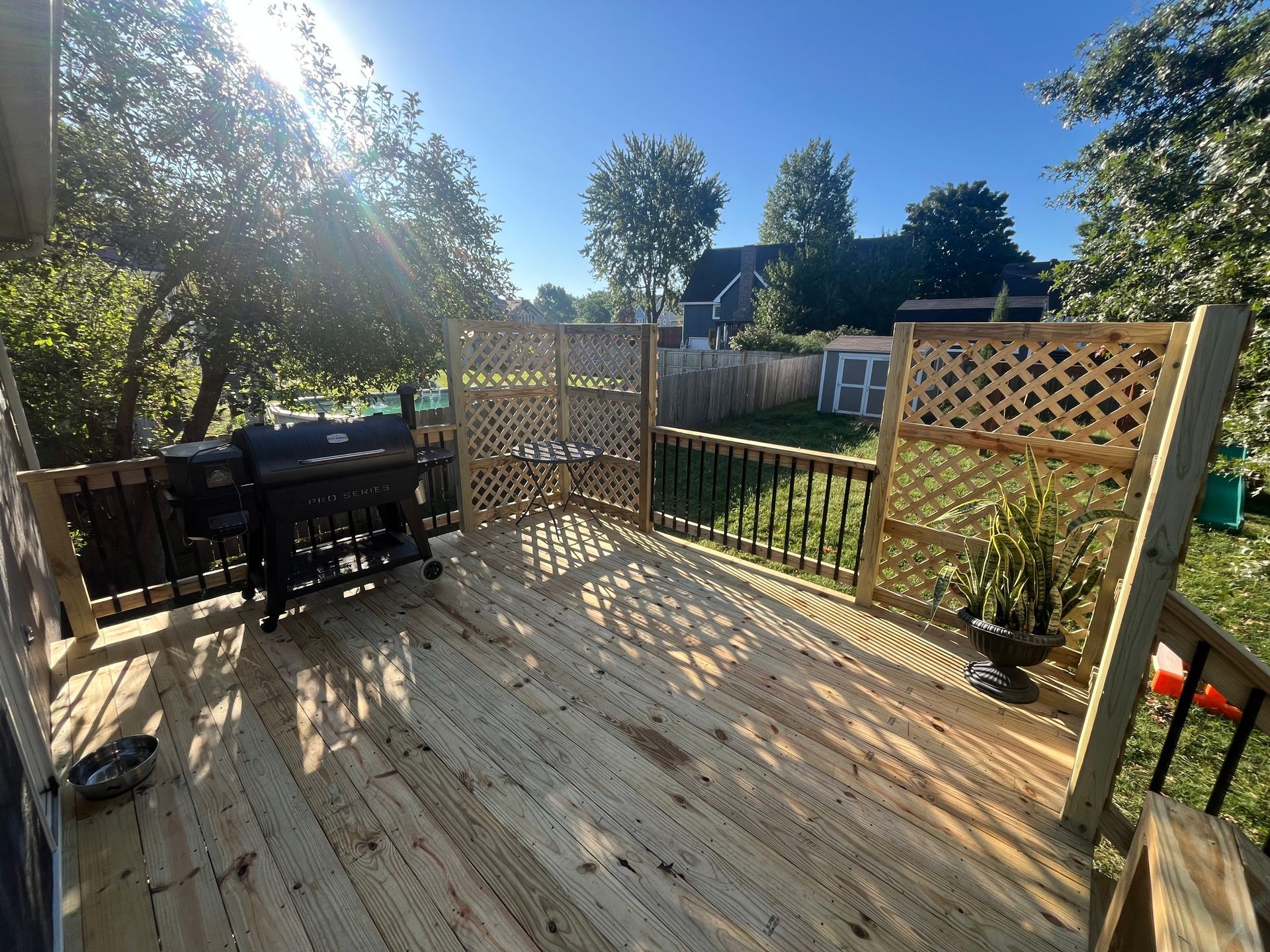 Wooden deck with grill and lattice screens, with a backyard view on a sunny day.