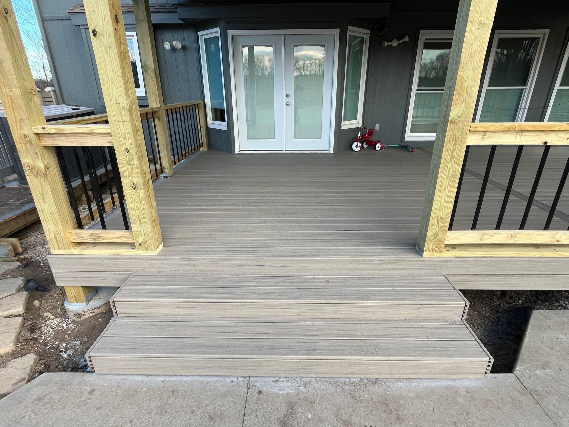 Wooden deck with steps leading to French doors, black railings, and light gray composite decking boards.