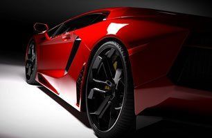 A red sports car with black wheels is parked on a white surface.