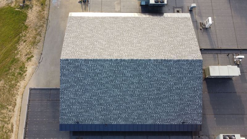 Overhead view of a building roof with two color sections: gray shingle and dark gray smooth.