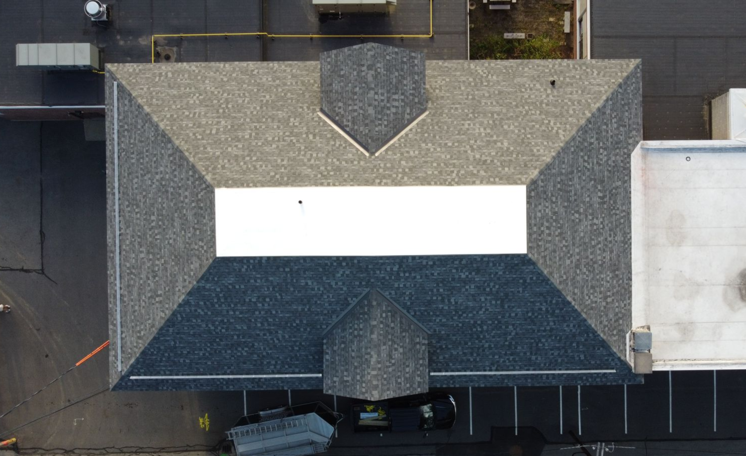 Overhead view of a building with a gray and white roof, surrounded by pavement.