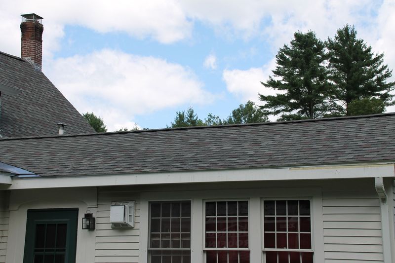 Gray-shingled roof and white building with windows, under a partly cloudy blue sky.