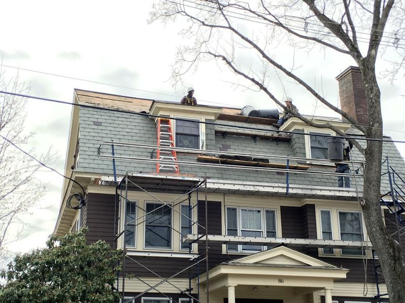 Roofers on a house with a slate roof, repairing shingles. Ladder and scaffolding present.