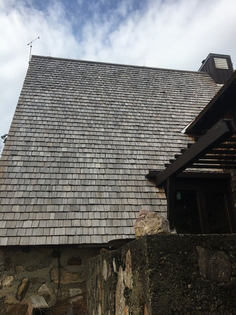 Wooden shingle roof on a building, a partial view, against a cloudy sky.