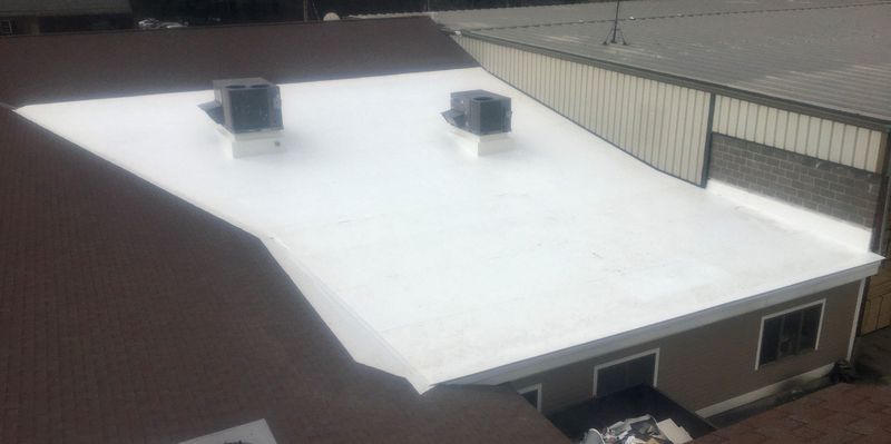 View of a white flat commercial roof with two square units, adjacent to a brown and gray building.