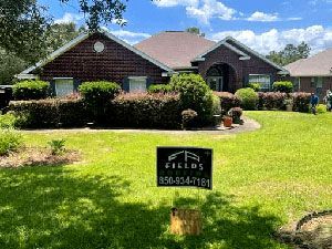 Brick house with red roof, trimmed hedges, and a lawn sign in the front yard.