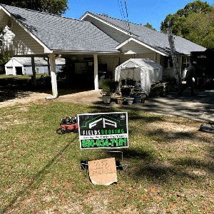 Front yard of a house with a greenhouse and a green-and-black real estate sign on the lawn.
