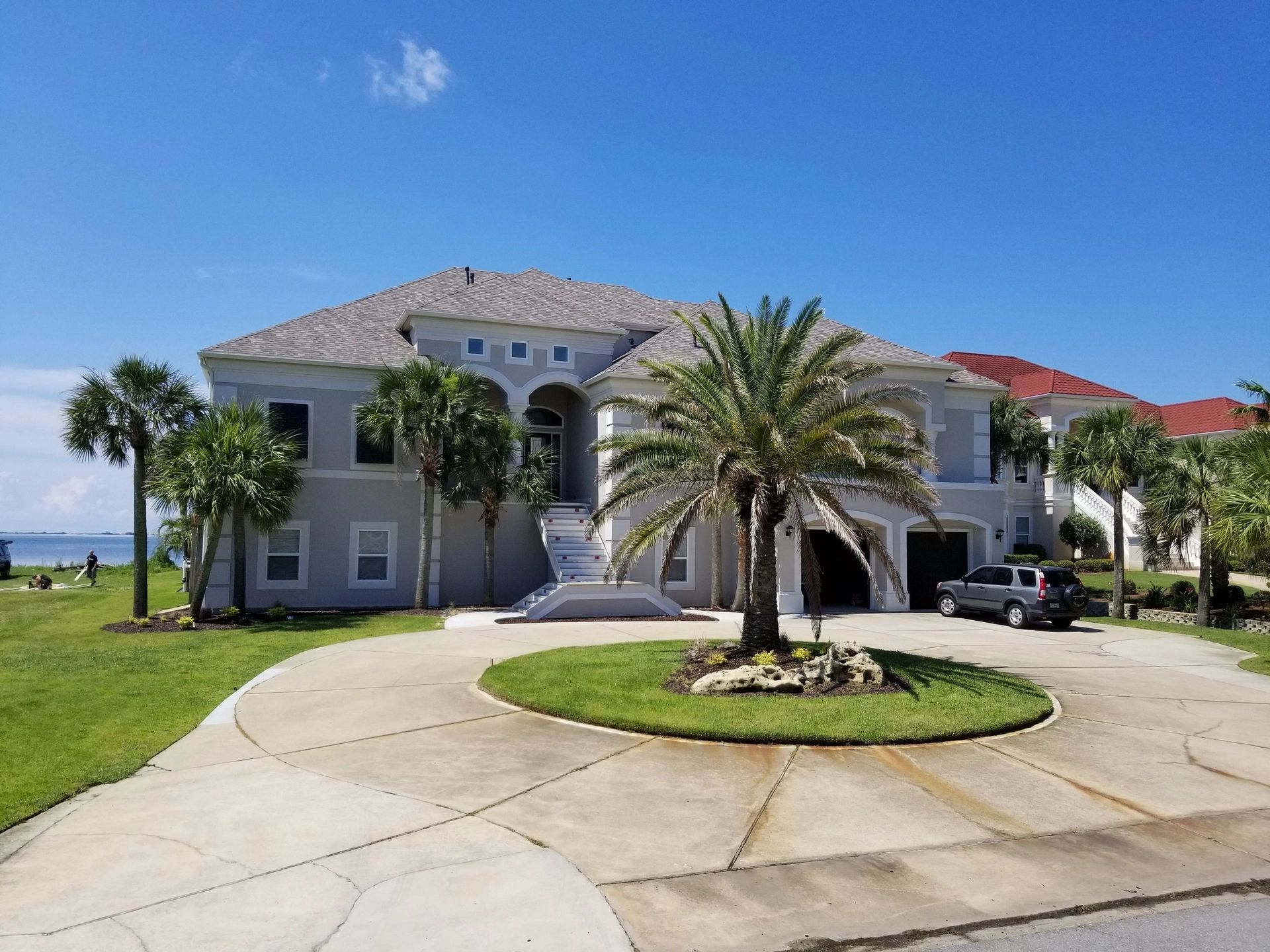 Luxury waterfront house with palm trees, circular driveway, and blue sky