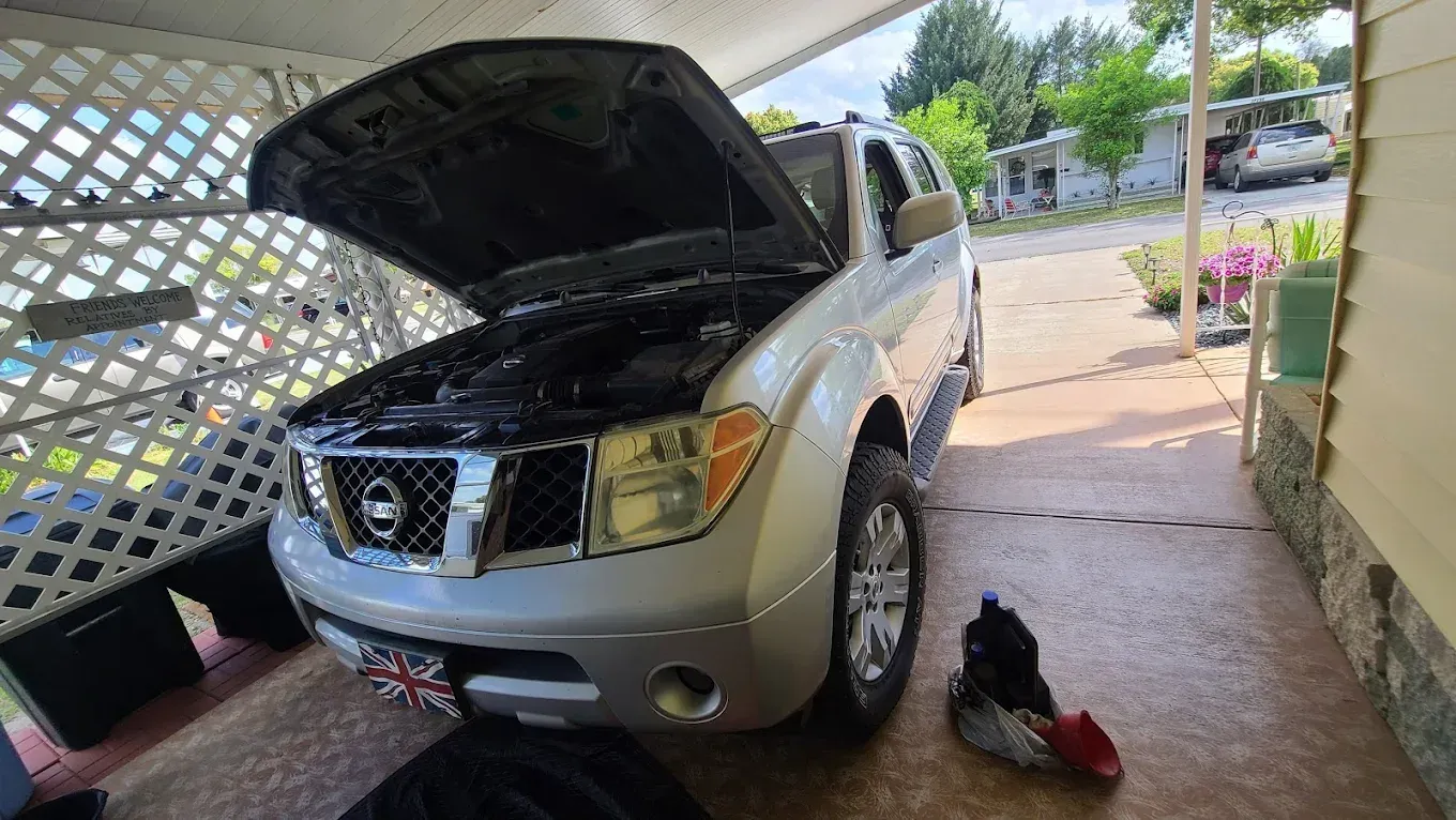 Silver Nissan Pathfinder with hood open, parked near a house with a carport.
