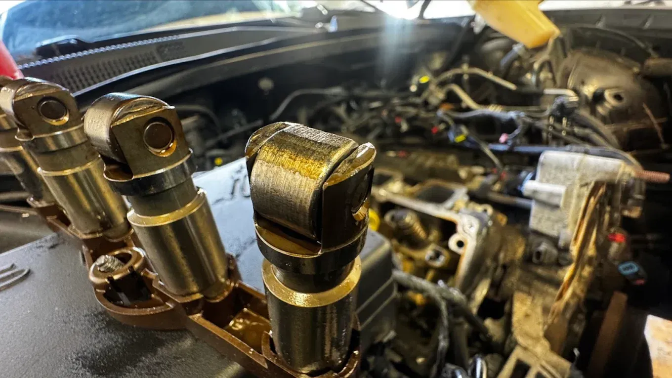 Engine lifters in a row, with a car engine in the background, likely in a garage.