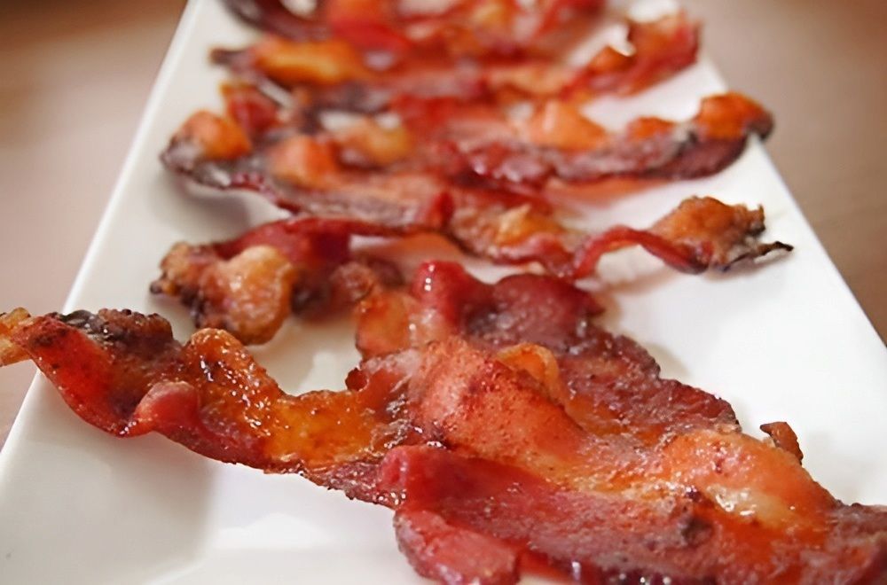 A White Plate Topped With Slices of Bacon on a Table — Corrado & Frank Distributors in Fairy Meadow, NSW