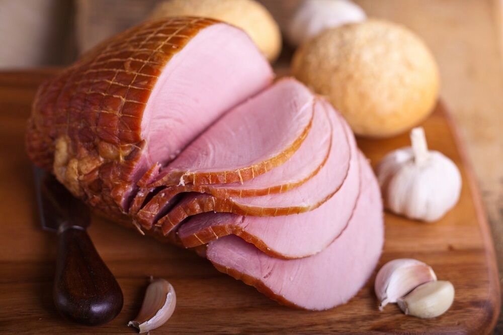 A Sliced Ham is Sitting on a Wooden Cutting Board Next to Garlic — Corrado & Frank Distributors in Fairy Meadow, NSW