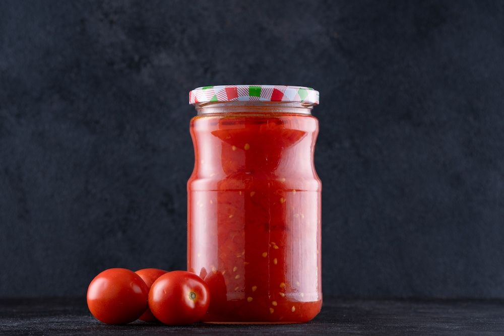 A Jar of Tomato Sauce Next to Some Tomatoes on a Table — Corrado & Frank Distributors in Fairy Meadow, NSW