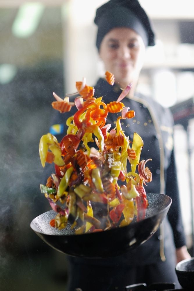 A Woman is Cooking Vegetables in a Wok in a Kitchen — Corrado & Frank Distributors in Southern Highlands, NSW