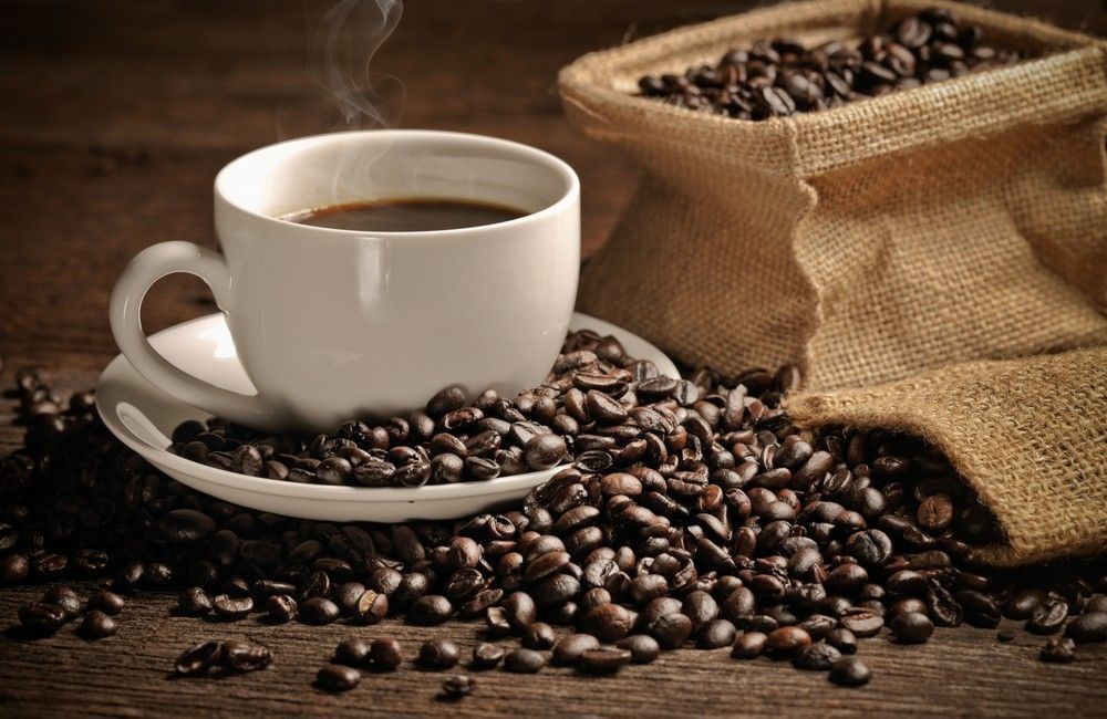 A Cup of Coffee is Sitting on a Saucer Next to a Bag of Coffee Beans — Corrado & Frank Distributors in Fairy Meadow, NSW