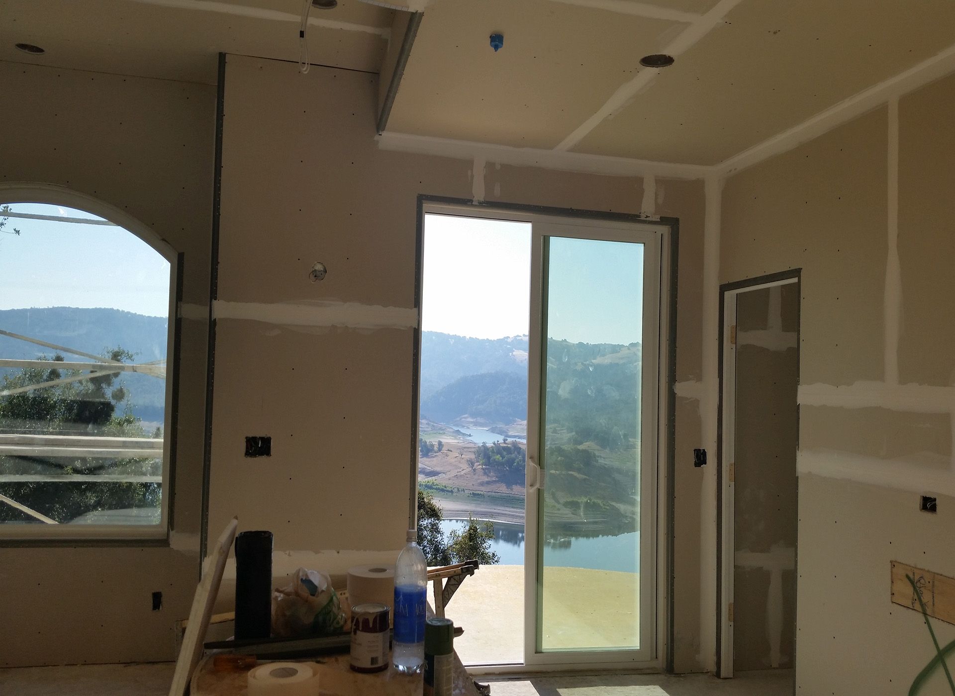 Unfinished room with large windows and a sliding glass door overlooking a lake and mountains