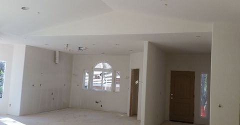Empty unfinished room with white walls, tiled floor, arched window, and wooden doors under construction