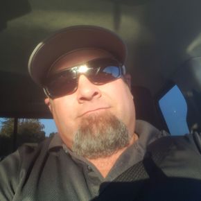 Man wearing a cap and sunglasses in a car, lit by sunlight.