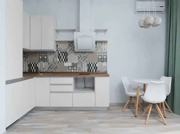 Minimal white kitchen with patterned backsplash, wood countertop, and small dining table with white chairs