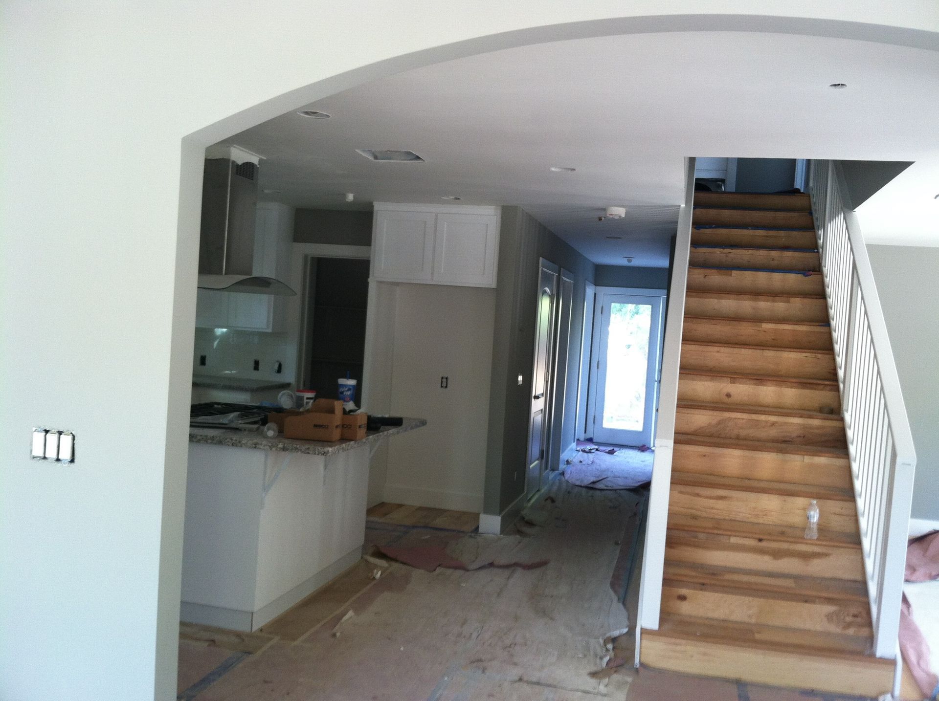 Interior of a house under renovation, with a kitchen area and wooden staircase leading upstairs.