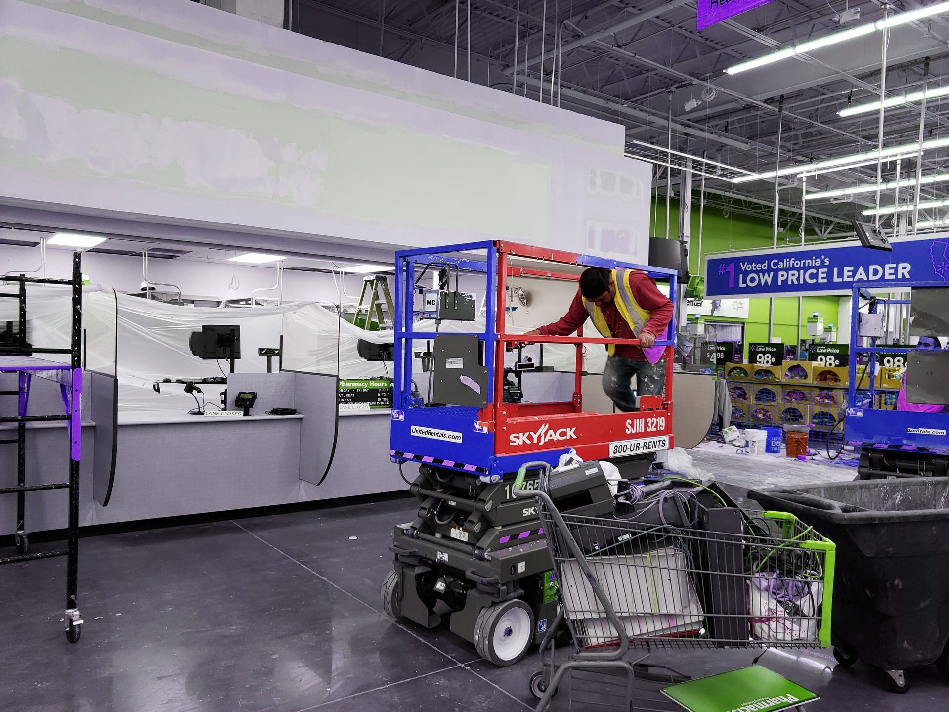 Blue-and-red scissor lift in a warehouse aisle with shelves, machinery, and a purple