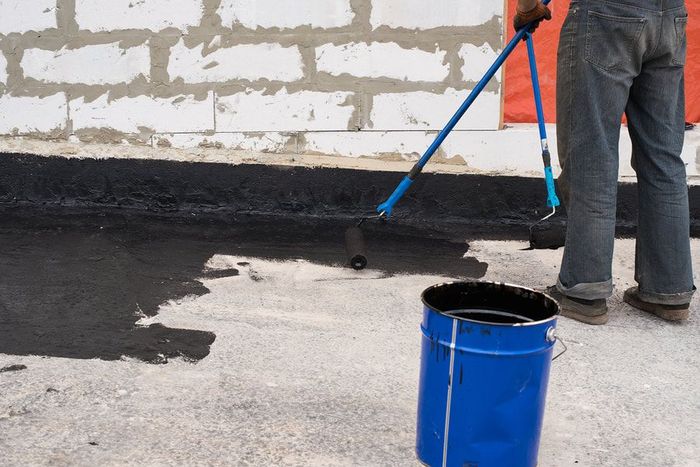 Maple Ridge Concrete employee providing sealing to a concrete driveway. The worker is wearing blue jeans and holding a rolling brush.