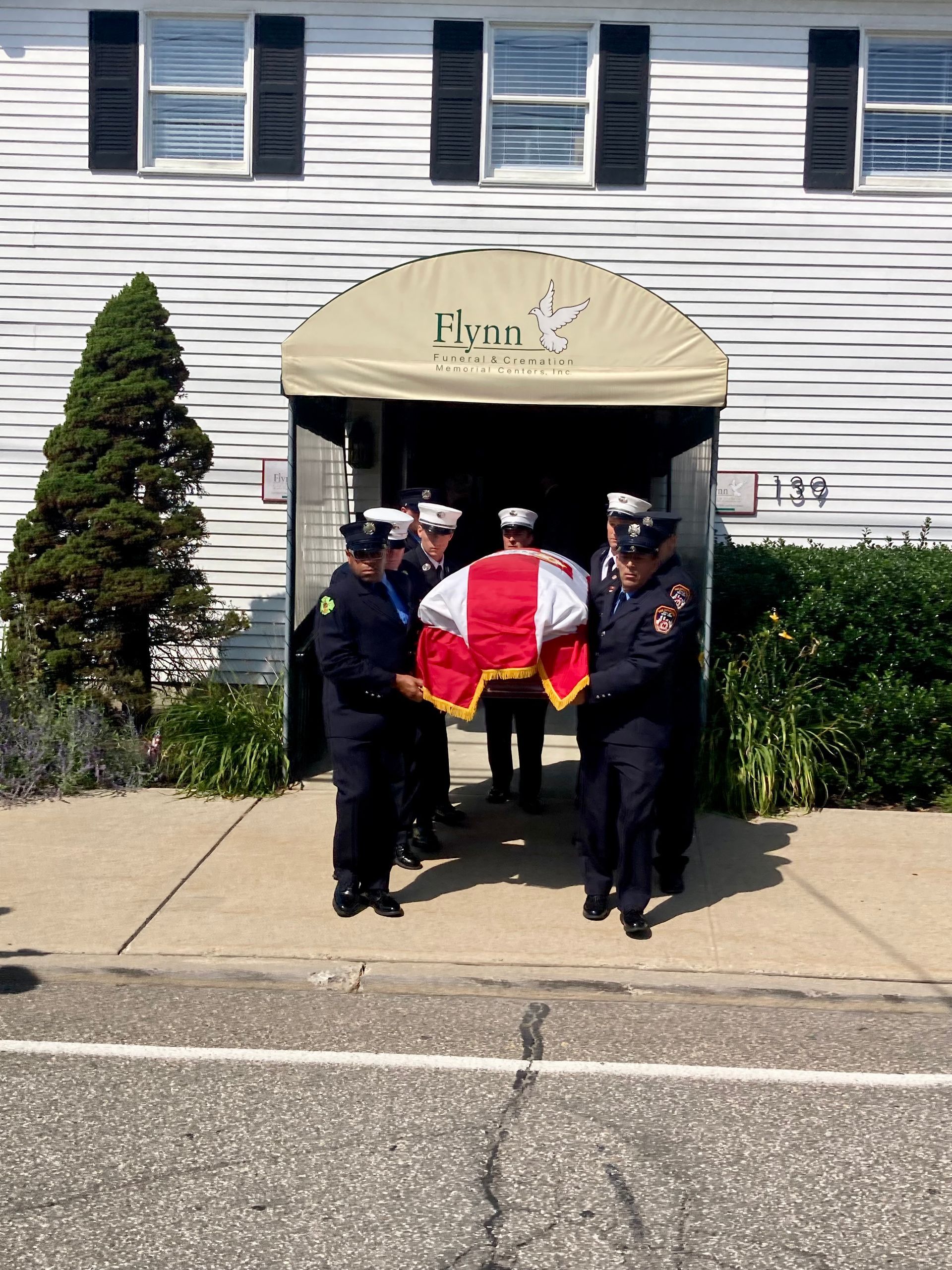 A man is standing in front of a coffin with flowers on it.