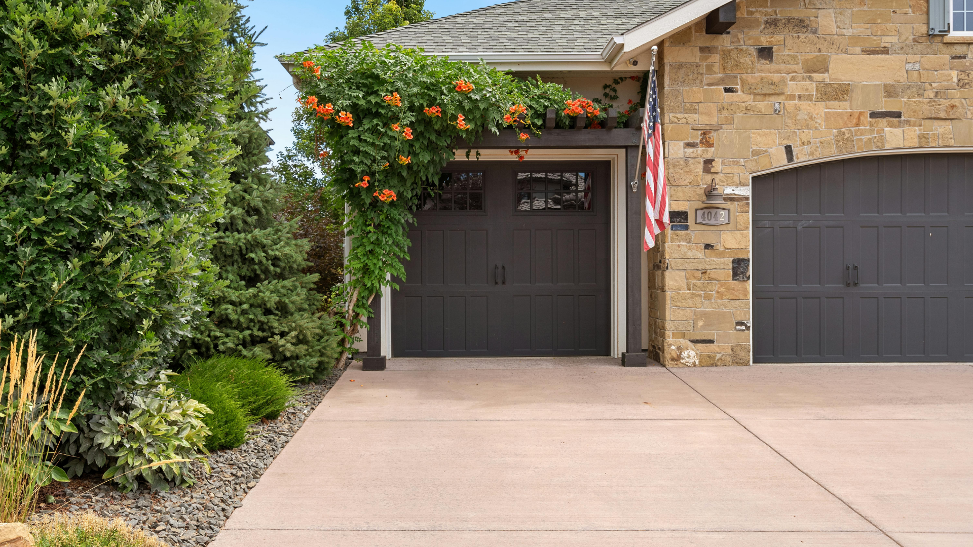 Front entrance of a house with dark garage doors, stone exterior, and orange flowering vines over the doorway