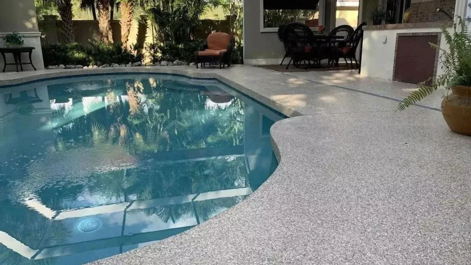 Backyard pool with blue water beside a textured patio and potted plants