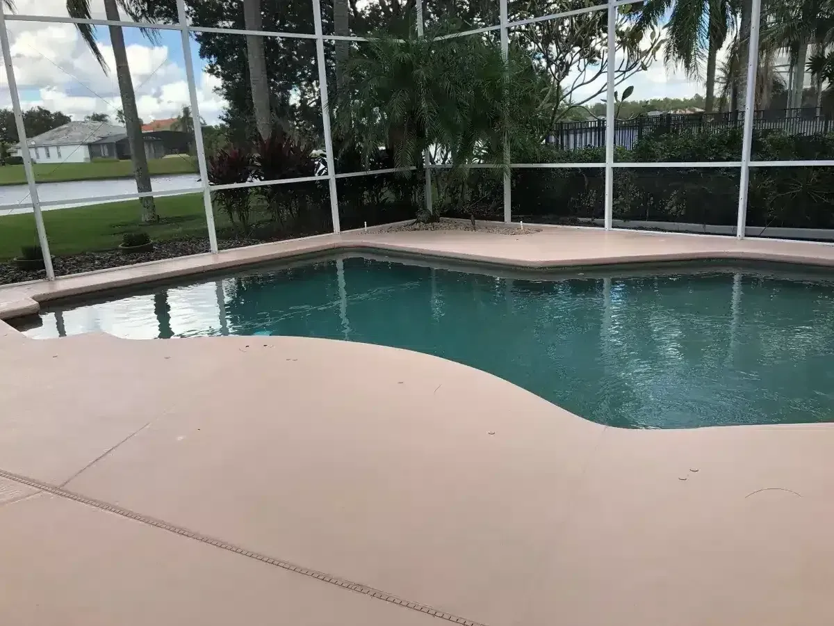 Screened backyard pool with turquoise water and tan deck beside a lawn and trees