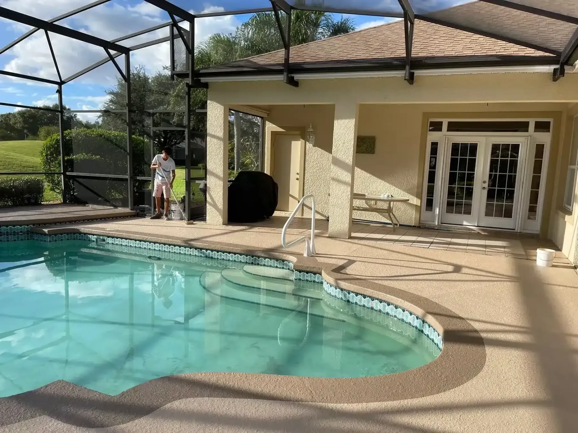 Backyard pool and screened patio beside a house with open French doors under a bright sky