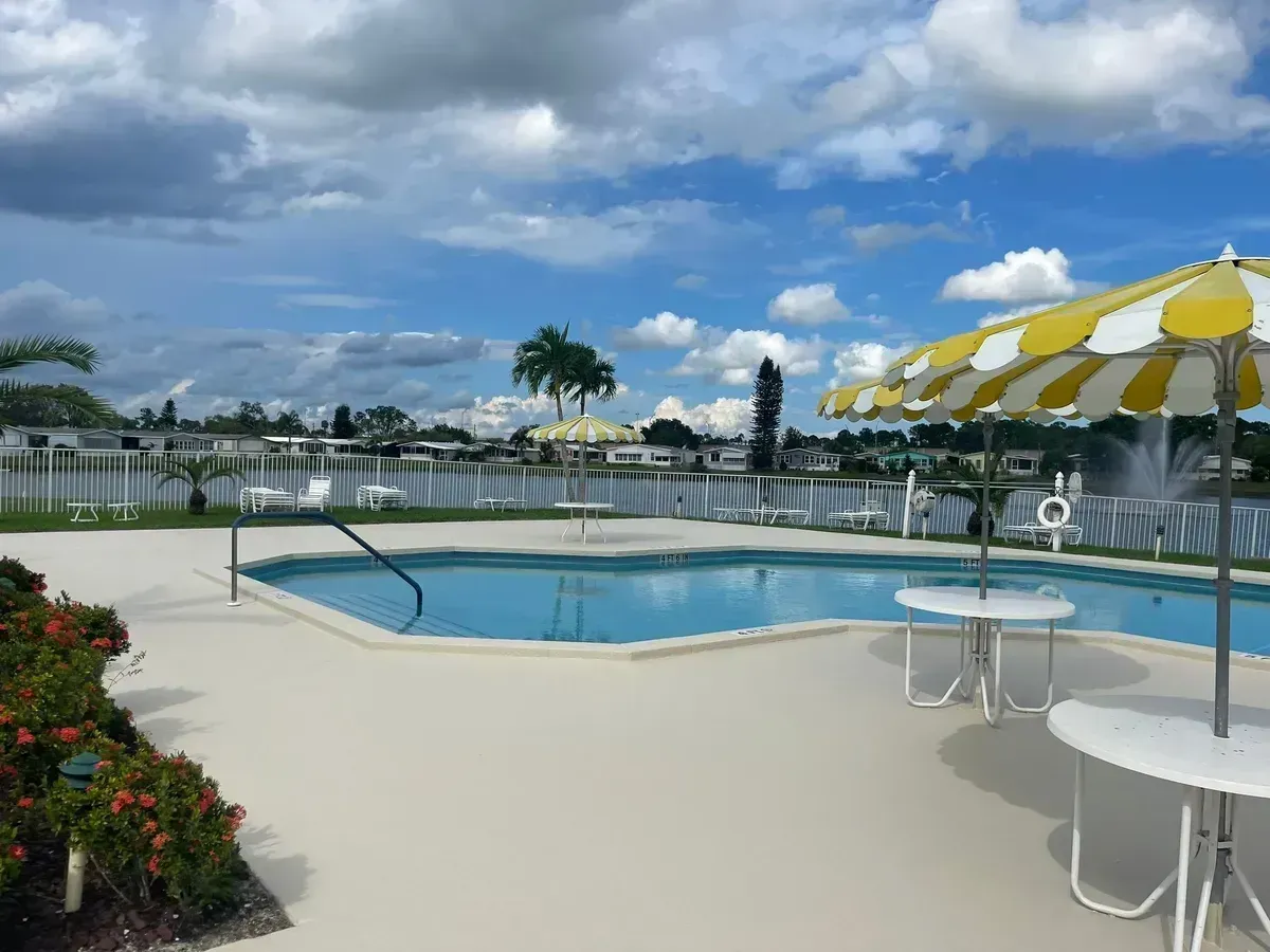 Outdoor pool with blue water, white lounge area, and yellow-and-white umbrellas under a cloudy sky