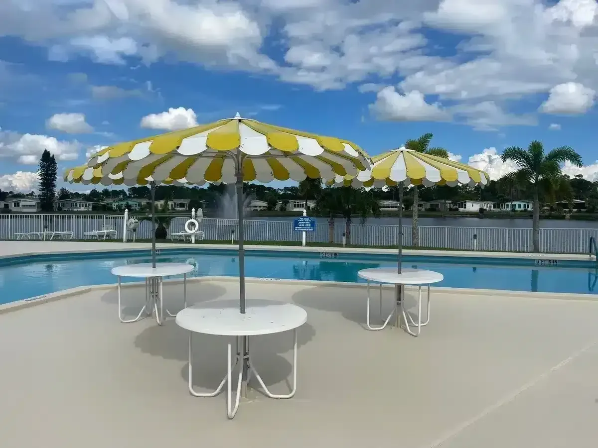 Poolside patio with yellow-and-white umbrellas and white tables under a blue, cloudy sky