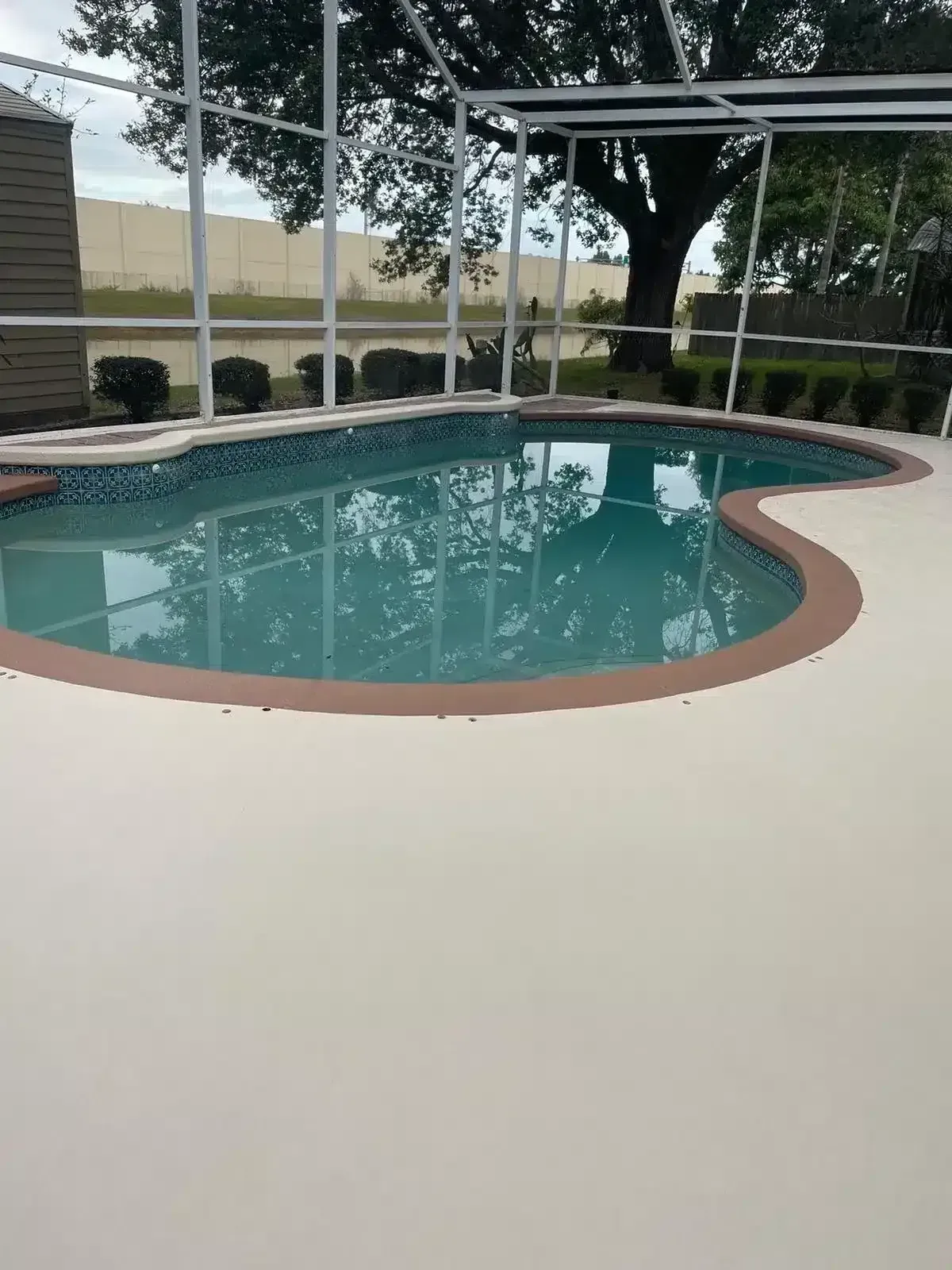 Backyard swimming pool with light blue water, surrounded by a concrete deck and covered patio seating area.