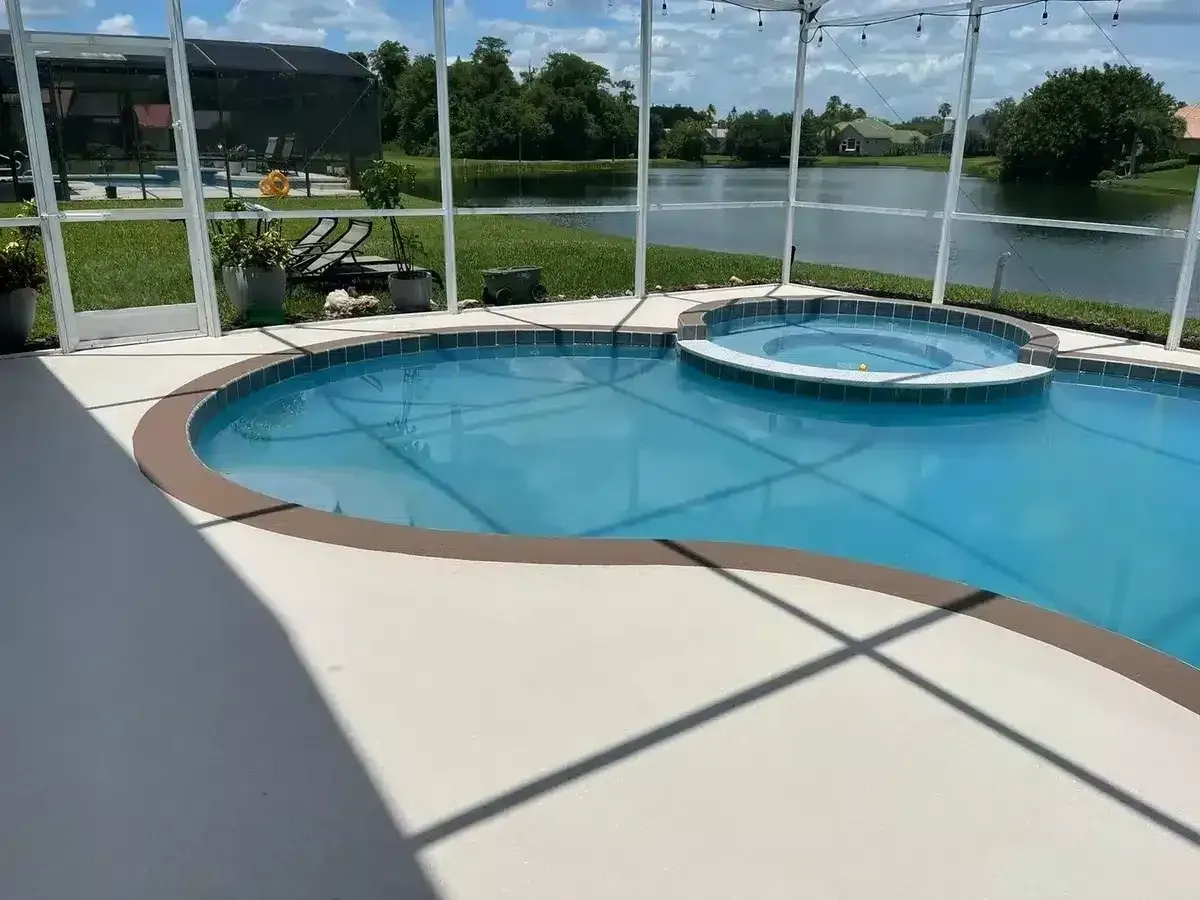 Screened patio with a curved pool and spa overlooking a lake, with lounge chairs nearby