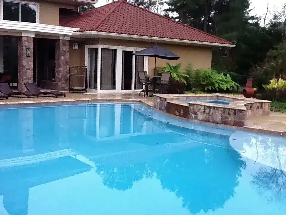 Backyard pool beside a house with a tan patio and red-tiled roof