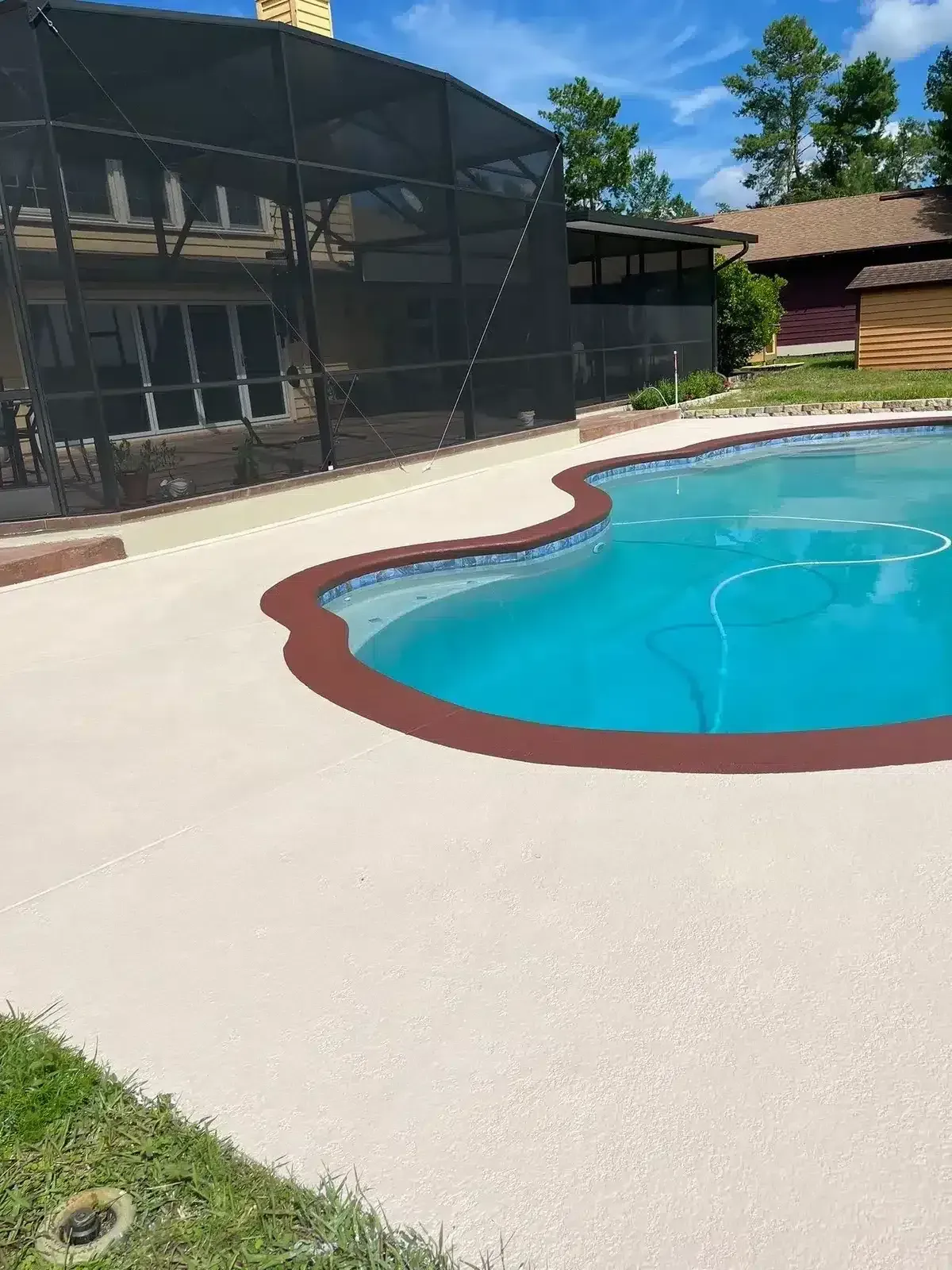 Backyard swimming pool with a tan deck and black screened enclosure under a blue sky