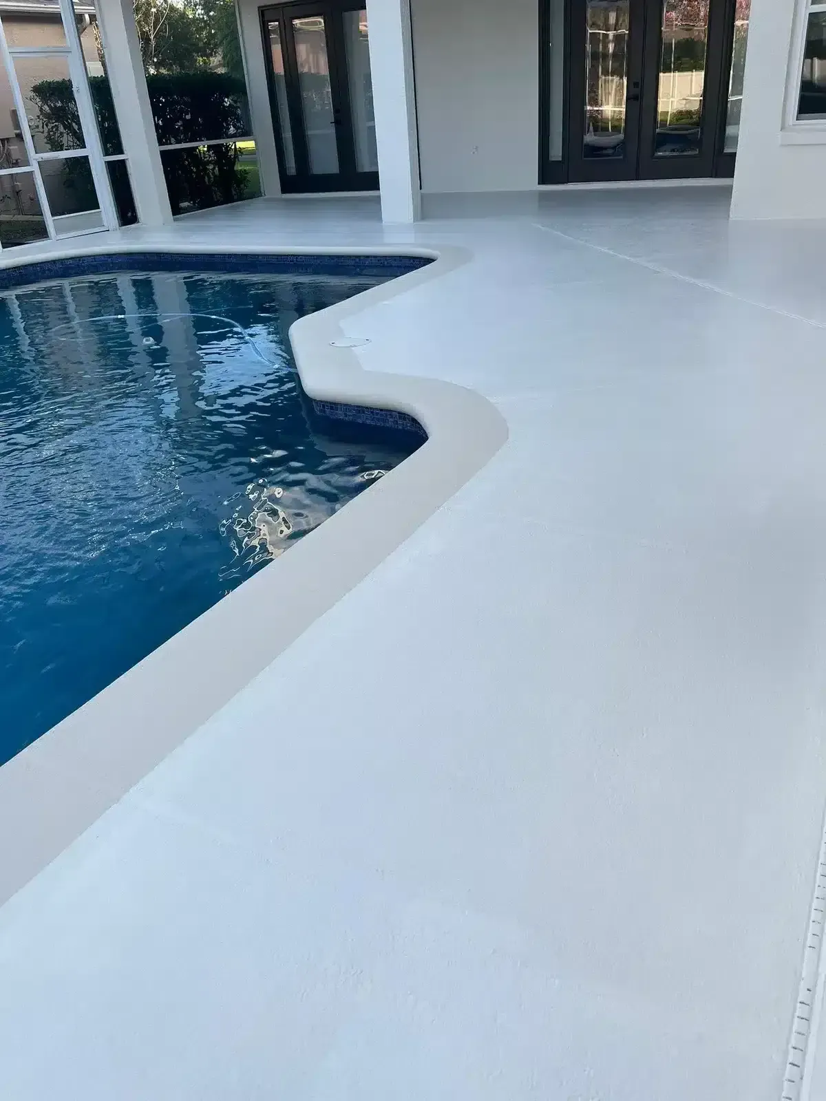 Curved pool edge beside a white patio with glass doors and outdoor seating area