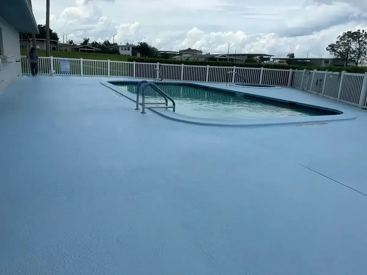 Blue pool deck with a small pool and metal handrails under a cloudy sky