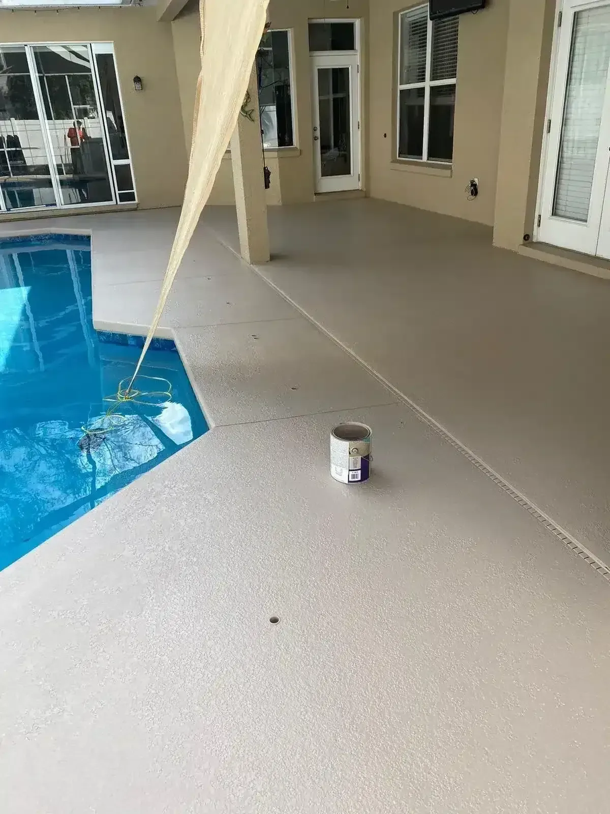 Painted pool deck with a paint can beside the swimming pool and house patio doors