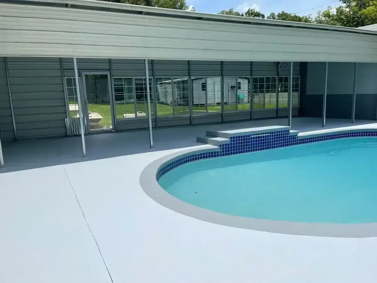 Outdoor swimming pool beside a modern building with glass doors and shaded patio area