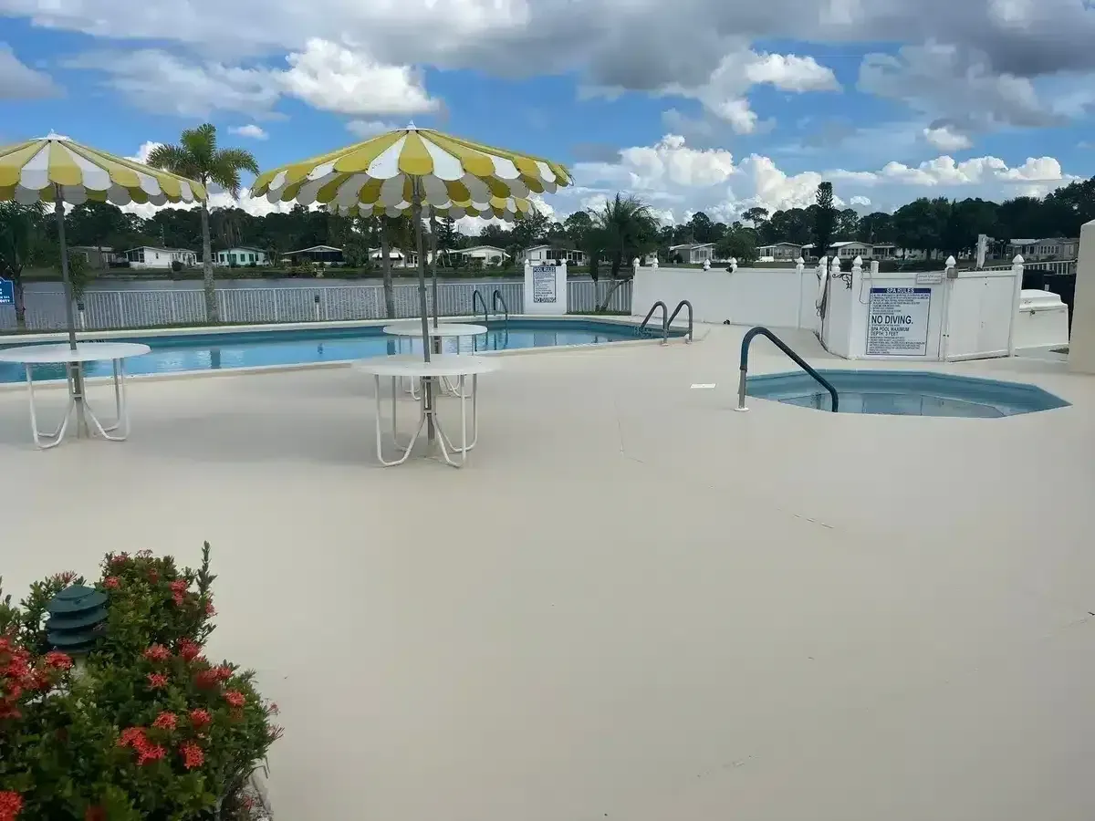 Empty outdoor pool with yellow-and-white umbrellas and blue lounge chairs under a cloudy sky